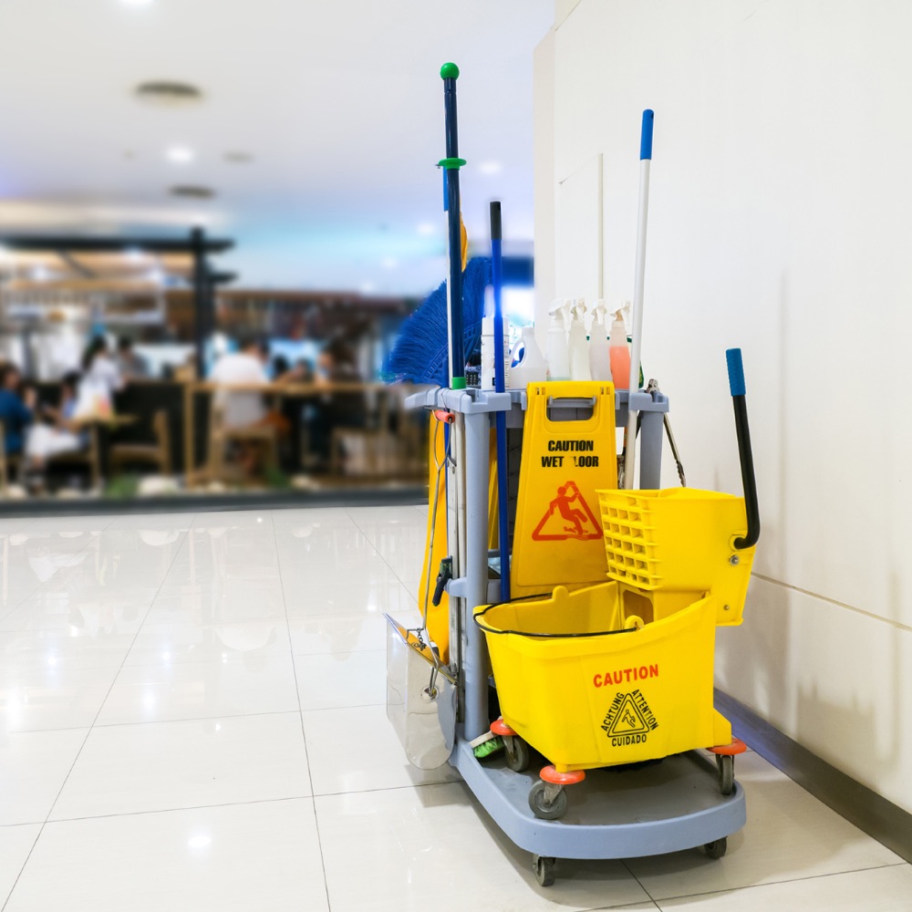 Janitorial cart with mop bucket, caution sign, and cleaning supplies in a bright commercial lobby