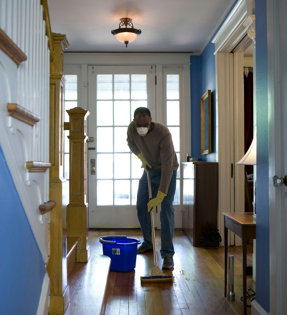 Cleaner in a dust mask mopping hardwood floors after a renovation